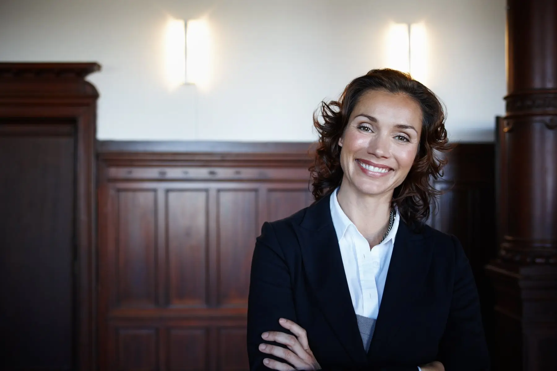 Une avocate souriante, bras croisés, dans un cabinet aux boiseries sombres