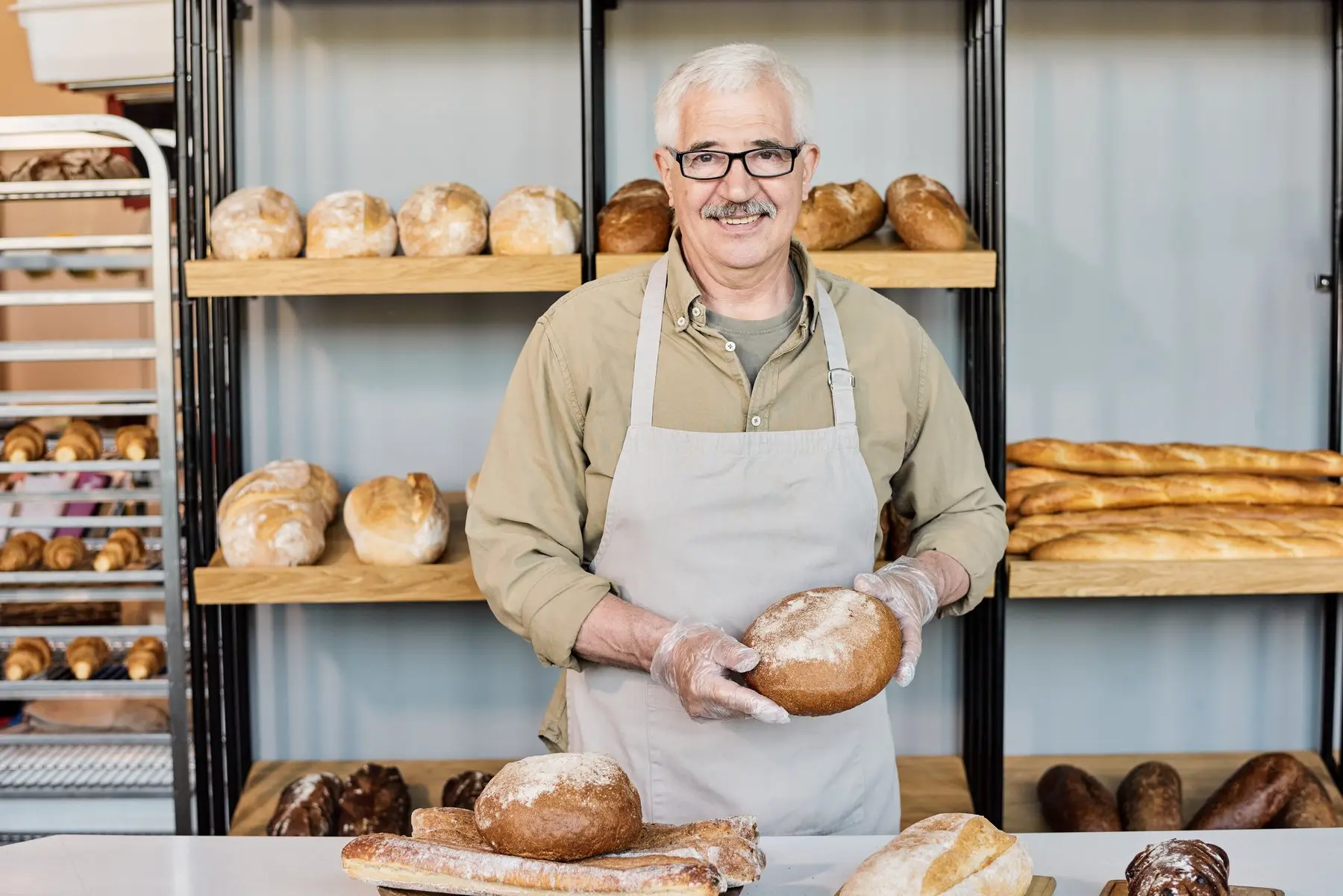 Un boulanger souriant présente une miche de pain devant ses étagères