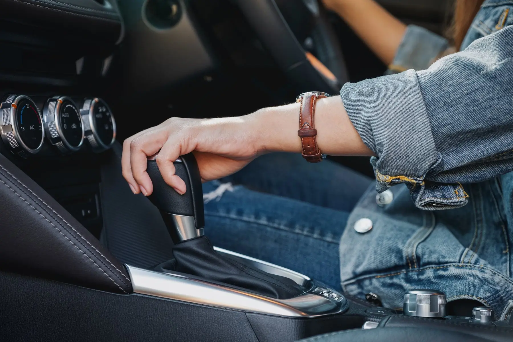 Gros plan sur la main d’une conductrice en veste en jean posée sur le levier d’une boîte automatique