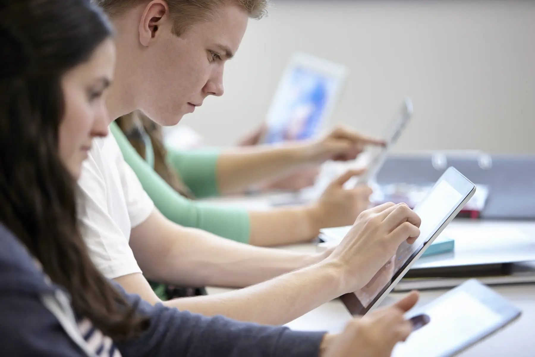 Des jeunes assis côte à côte s’entraînent sur des tablettes dans une salle claire