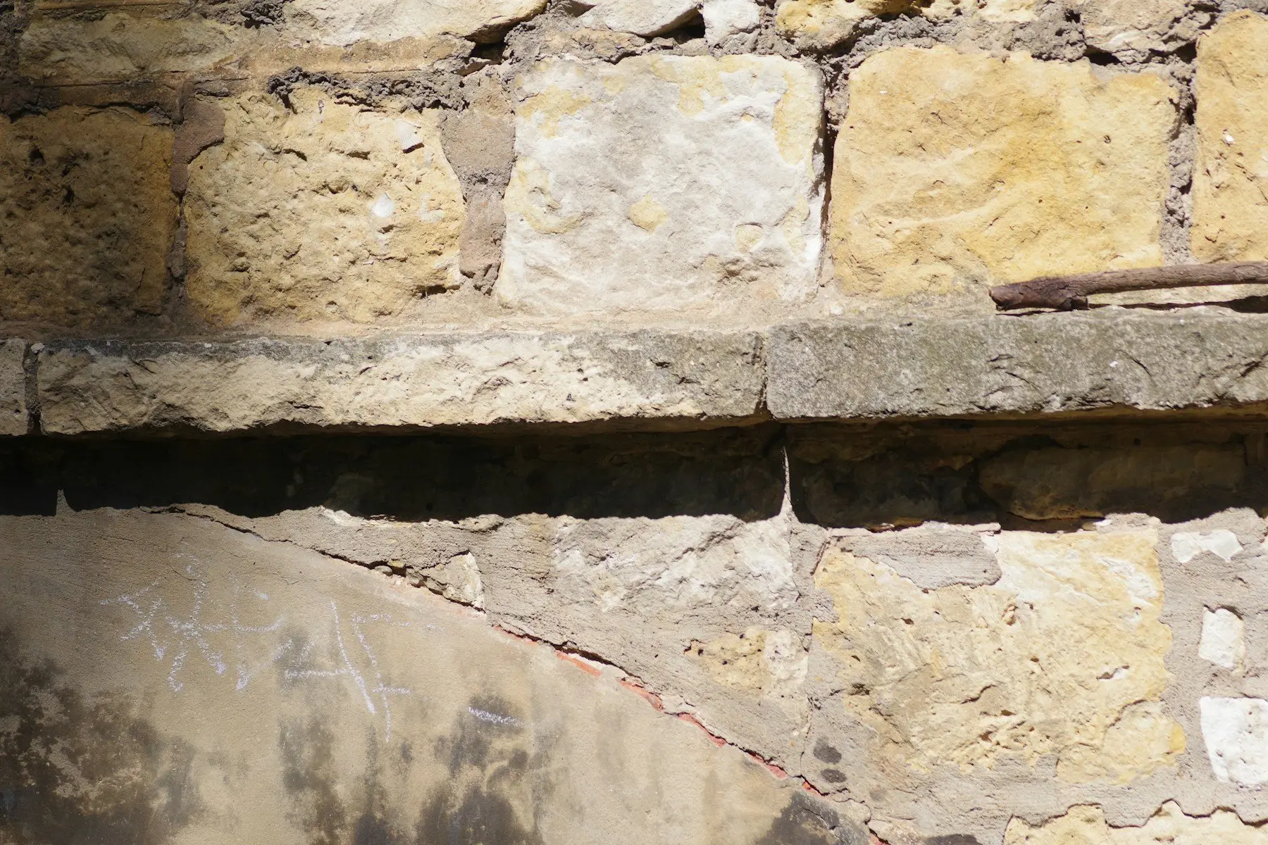 Gros plan d’un mur de pierre aux joints usés, traversé par une fissure qui part sous un linteau