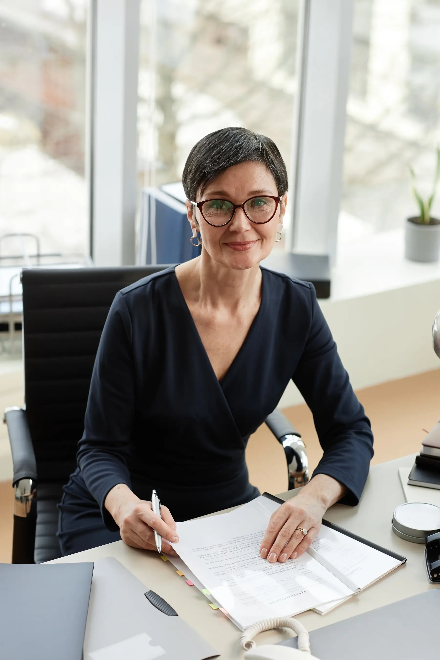Portrait d’une experte-comptable aux cheveux courts et lunettes rouges, assise à son bureau devant un dossier ouvert