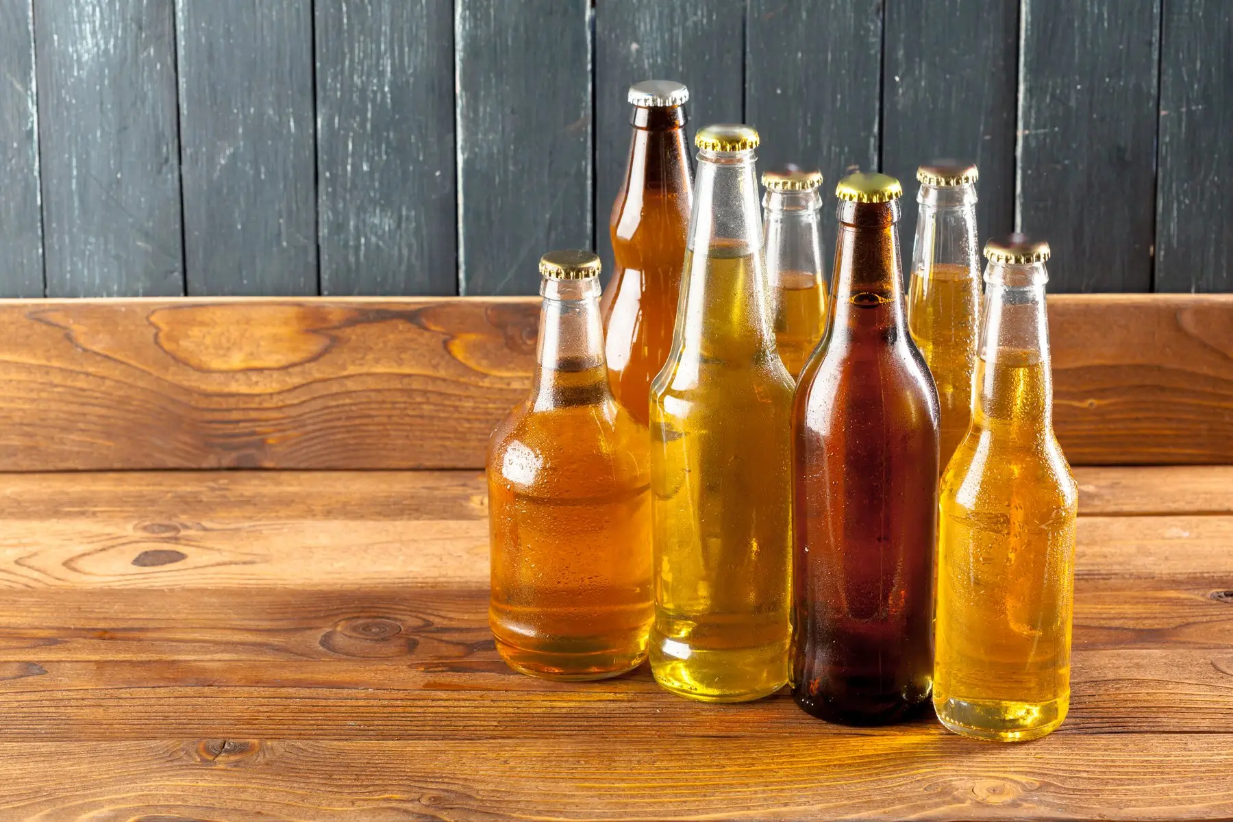 Sept bouteilles de bière blondes et ambrées alignées sur une table en bois brut