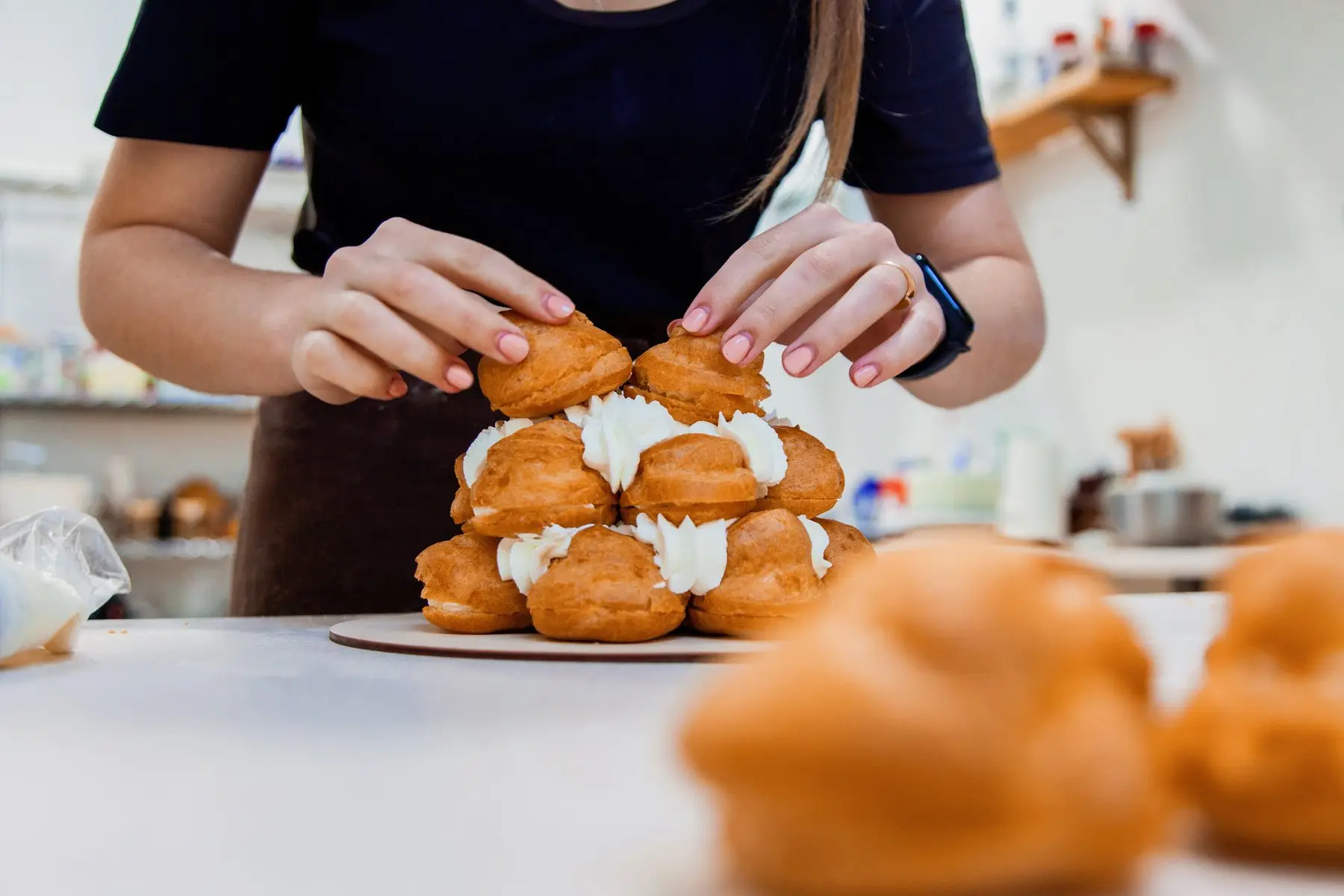 Une pâtissière assemble une pièce montée en choux garnis de crème, sur un plan de travail