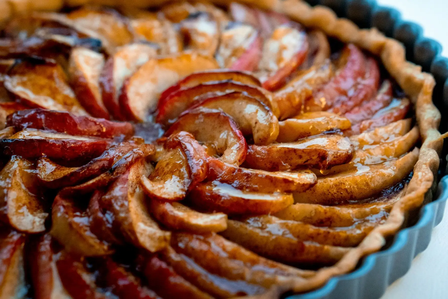 Tarte aux pommes vue de près, lamelles de pommes caramélisées disposées en rosace dans un moule cannelé