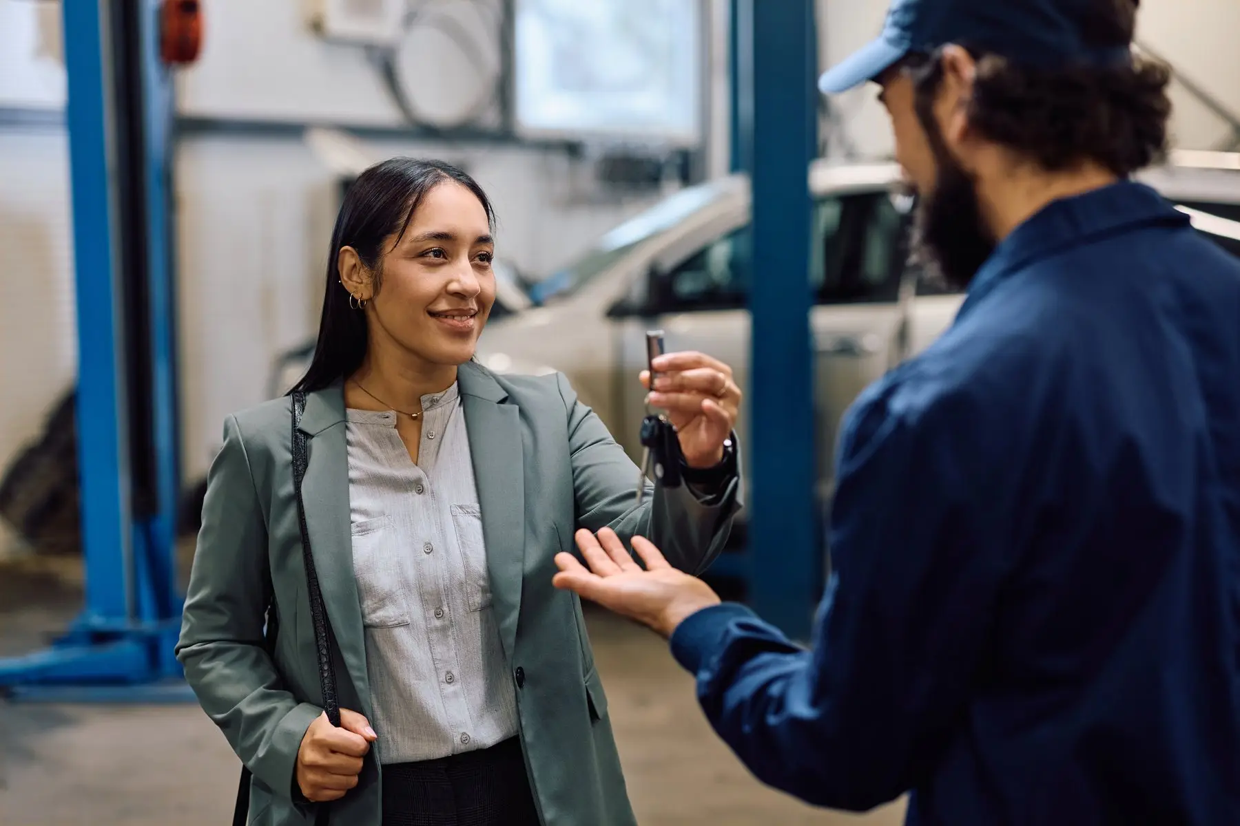 Une cliente souriante tend ses clés de voiture à un mécanicien en bleu de travail, dans l’atelier