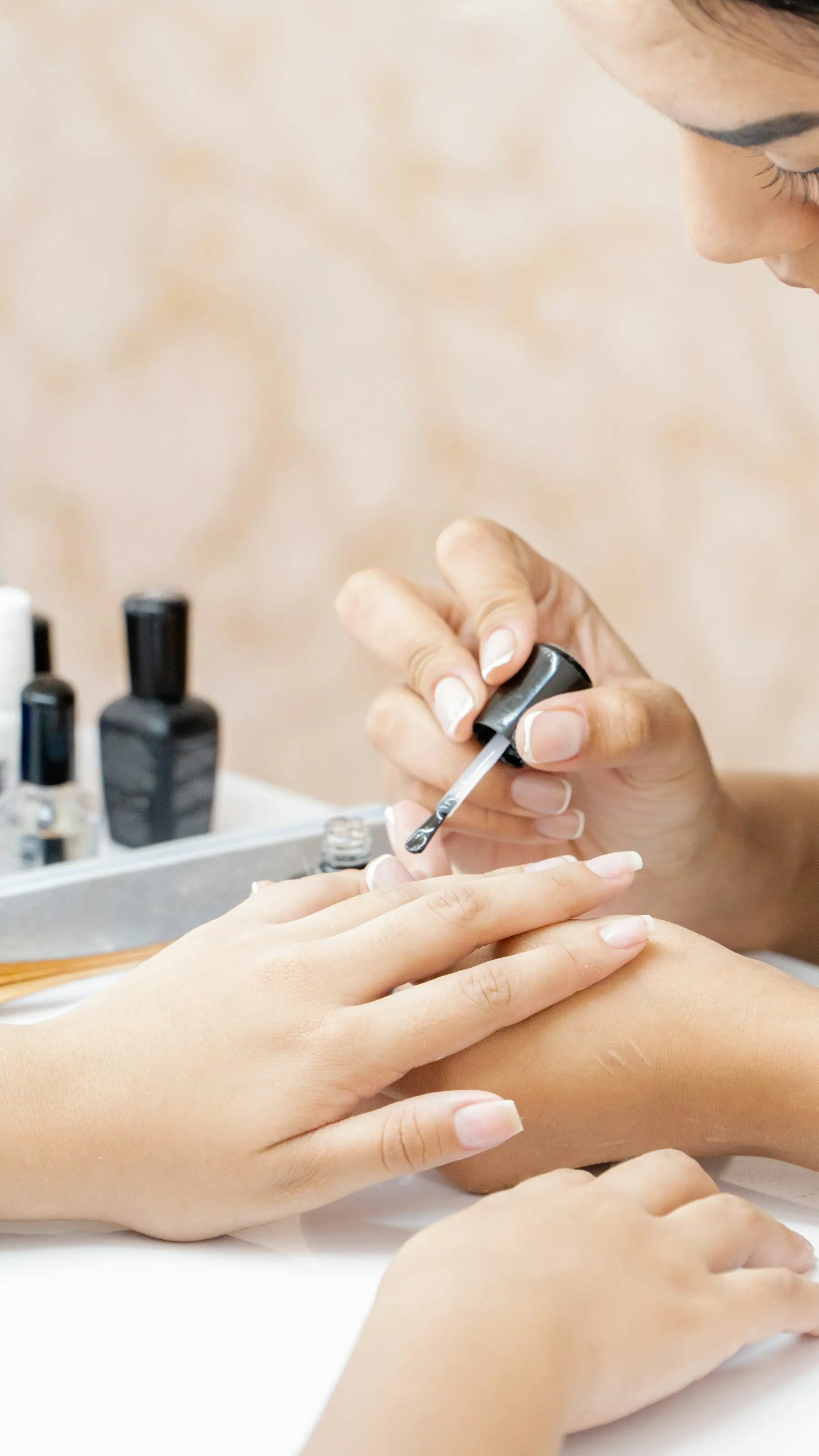Pose de vernis transparent sur les ongles d’une cliente, flacons de vernis posés sur la table