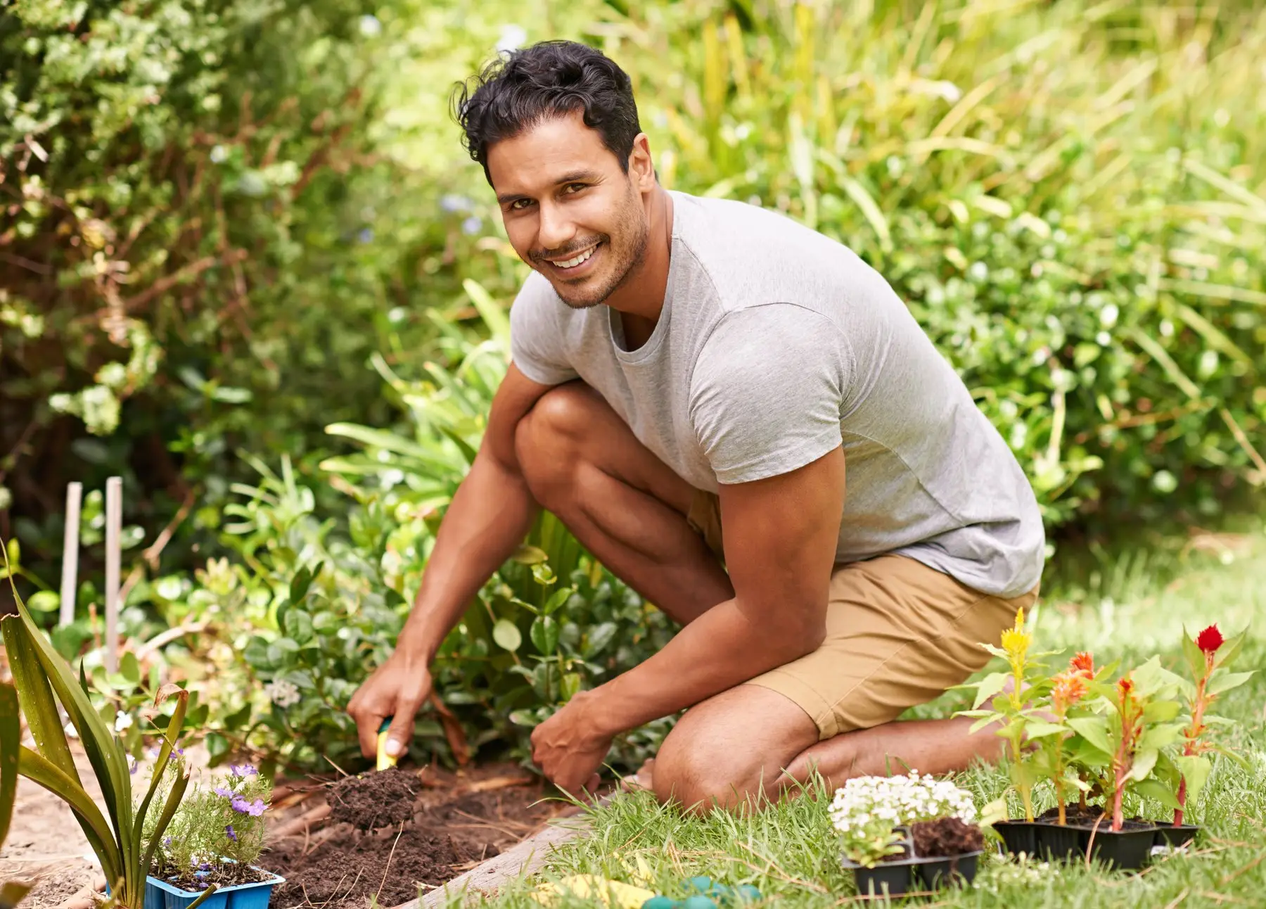 Un jardinier souriant, à genoux dans un massif, plante de jeunes fleurs