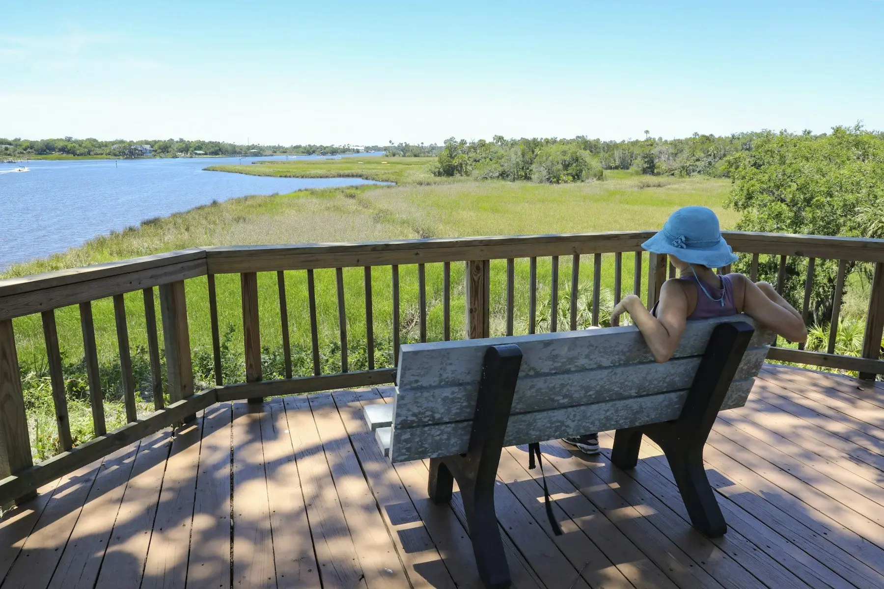 Terrasse en bois avec garde-corps et banc, face à l’eau et aux prés bordés de roseaux