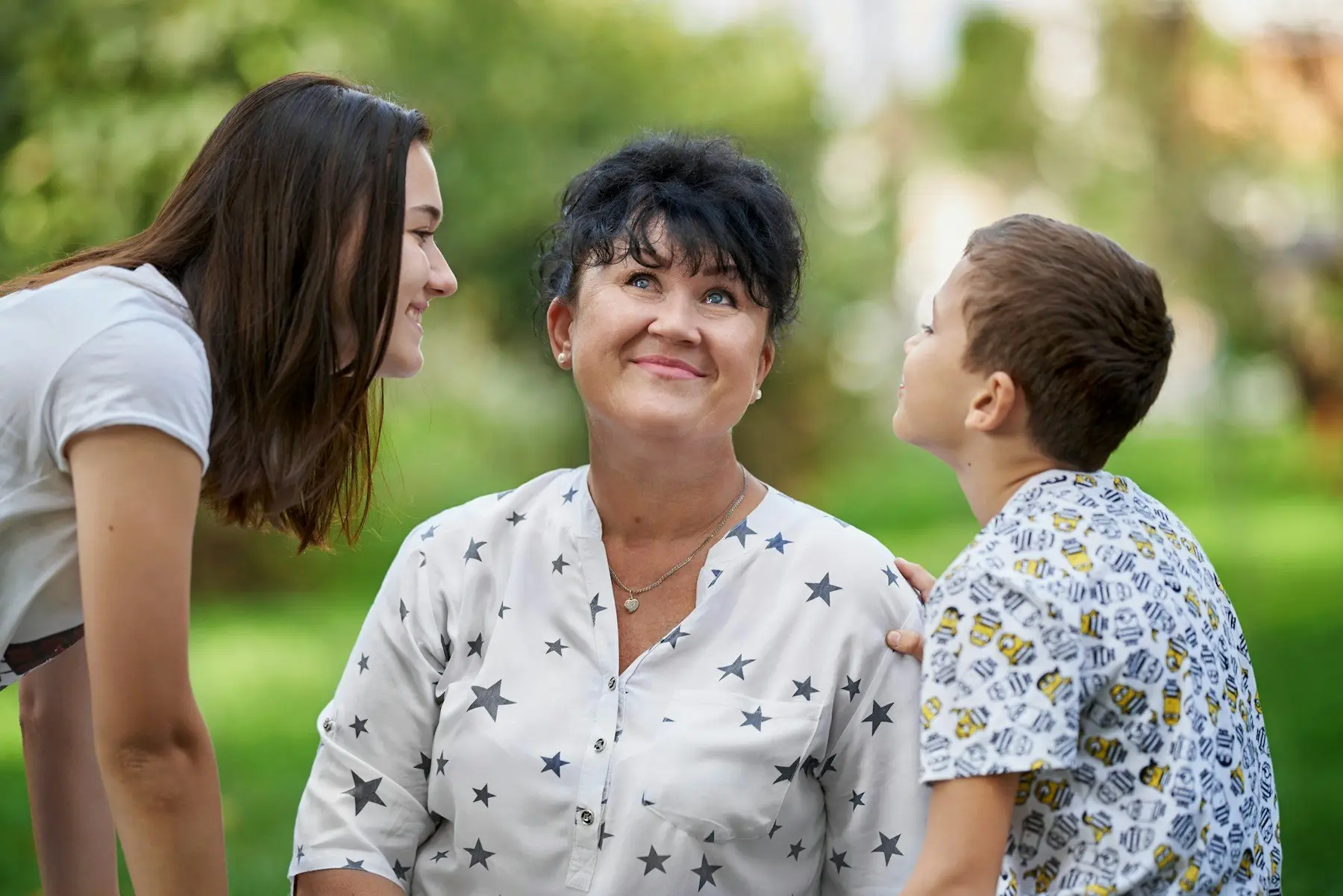 Une femme souriante lève les yeux vers une adolescente et un jeune garçon, dans un jardin