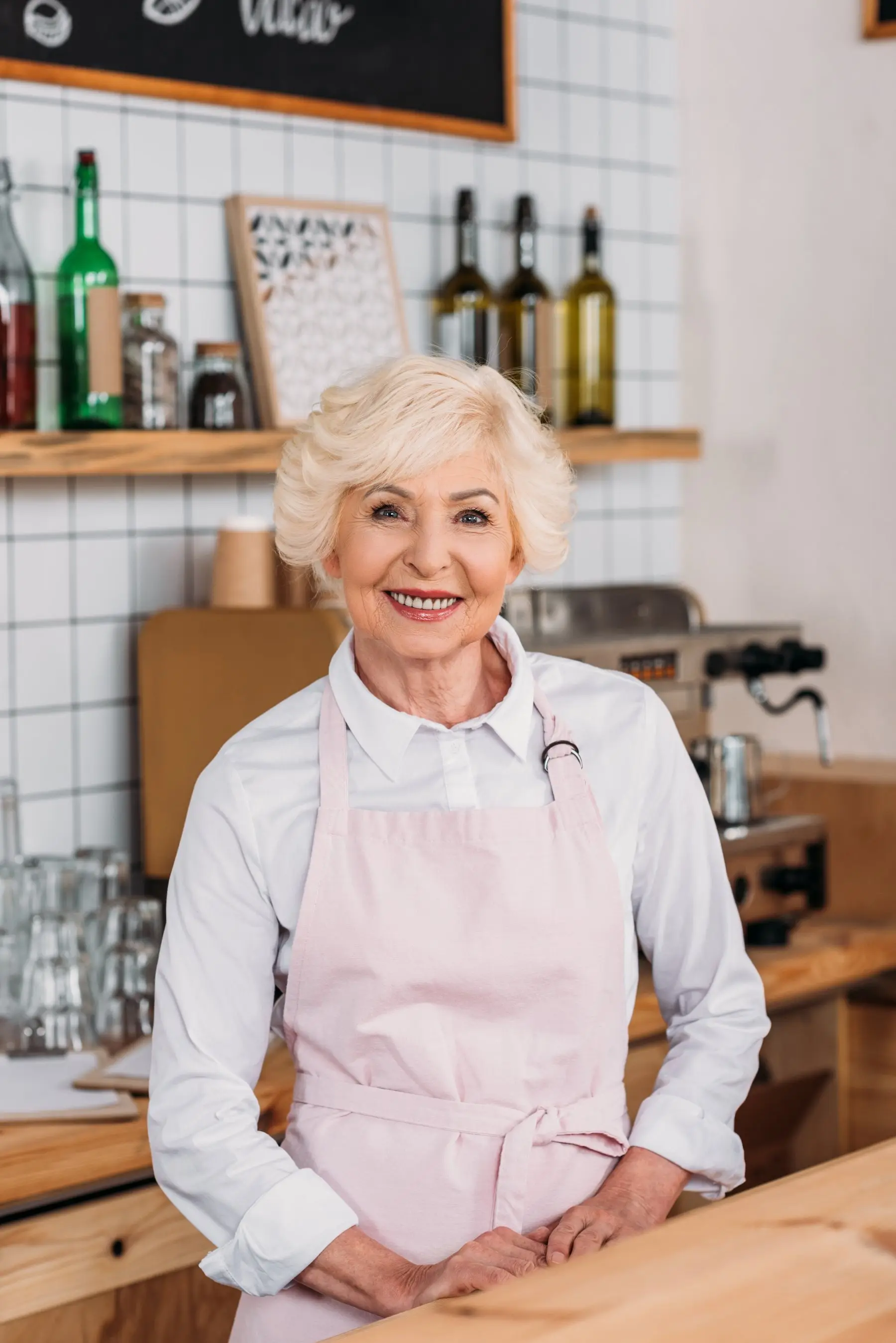 Une crêpière aux cheveux blancs, en tablier rose, sourit derrière son comptoir