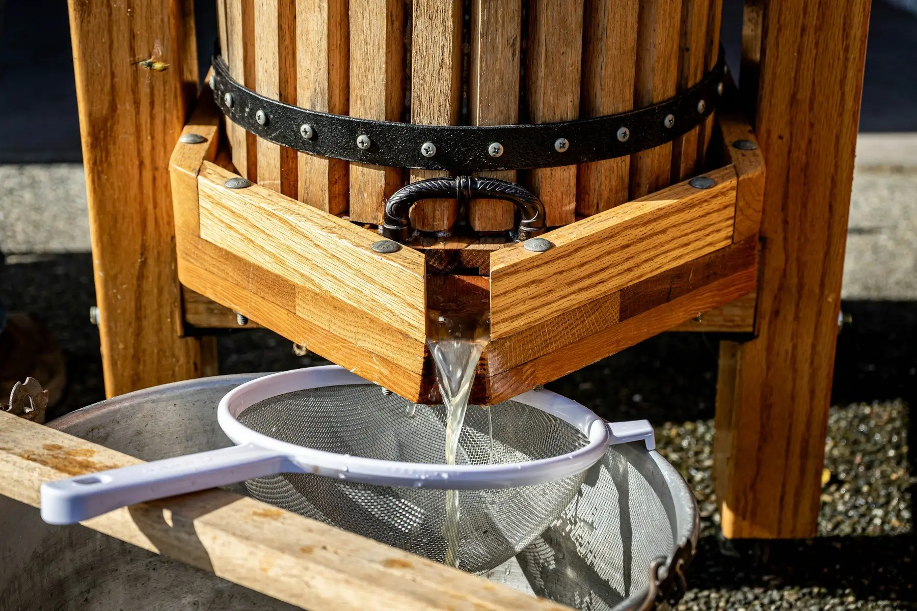 Du jus de pomme coule d’un pressoir en bois dans une passoire posée sur un seau