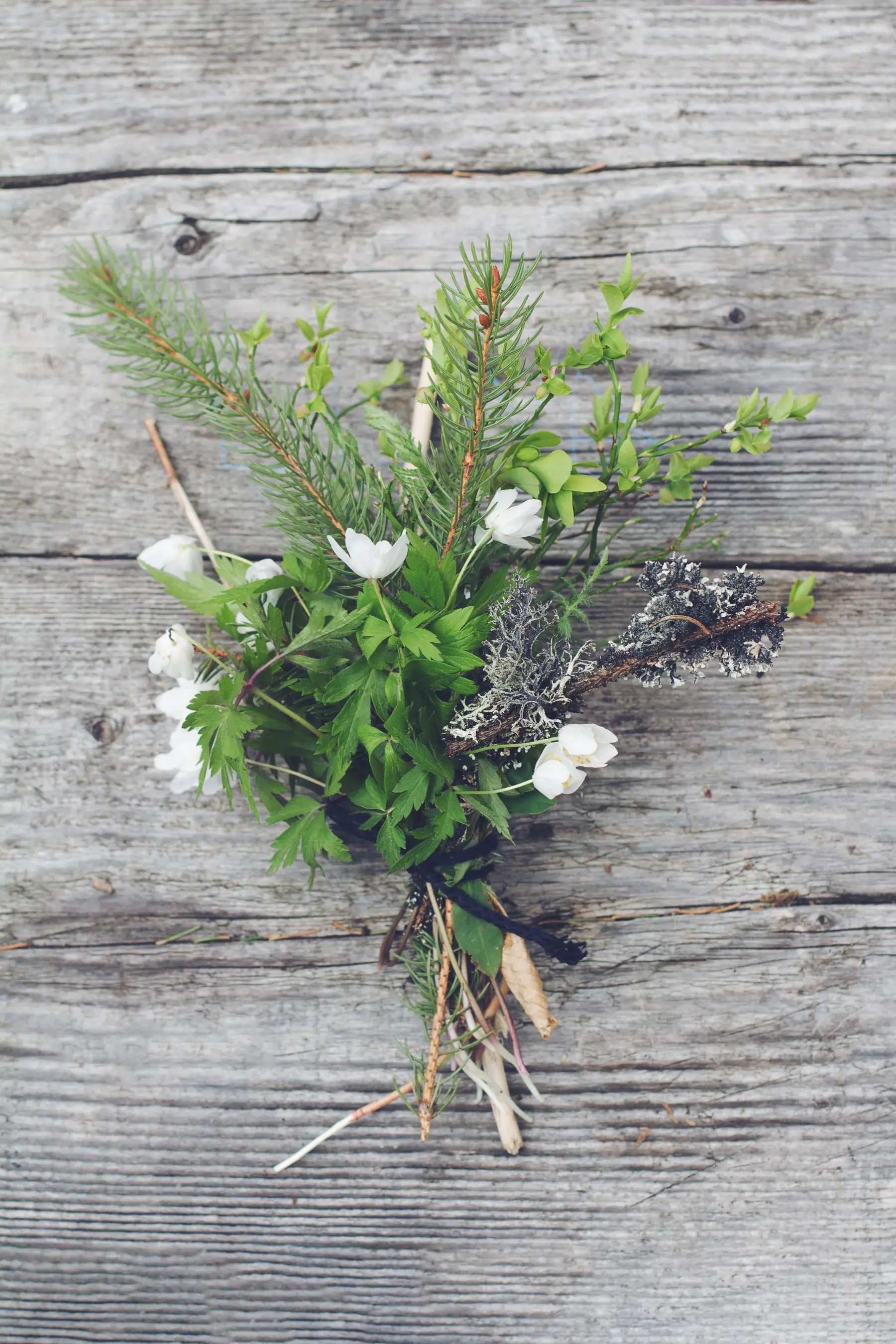 Petit bouquet de fleurs blanches, de branches de sapin et de lichen, noué d’une ficelle noire et posé sur un plancher gris