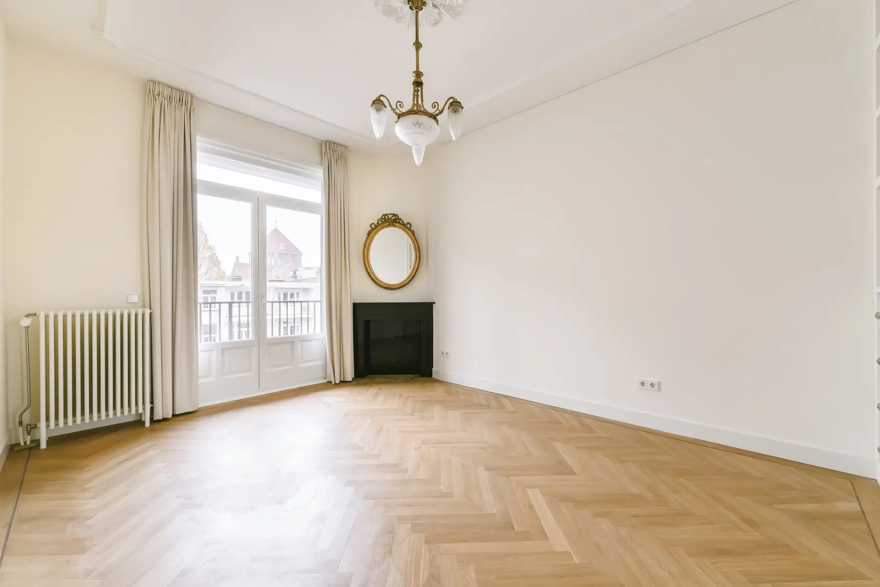 Pièce vide et lumineuse, parquet en point de Hongrie, cheminée noire, miroir doré et lustre ancien