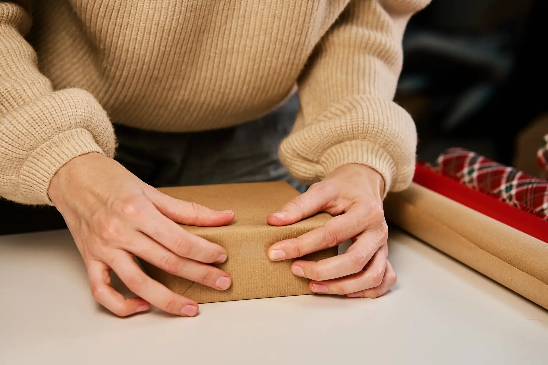 Mains emballant un petit paquet dans du papier kraft, rouleaux de papier cadeau à côté