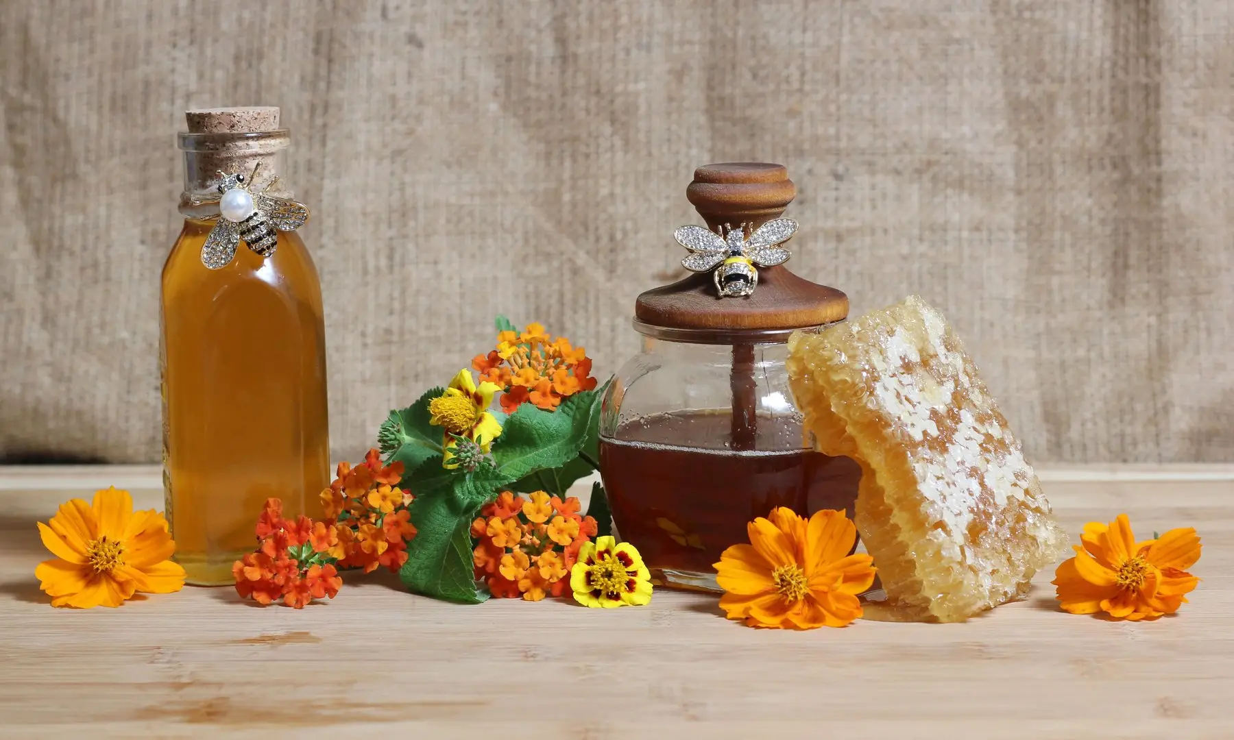 Bouteille et pot de miel, rayon de miel et fleurs orangées posés sur une table en bois