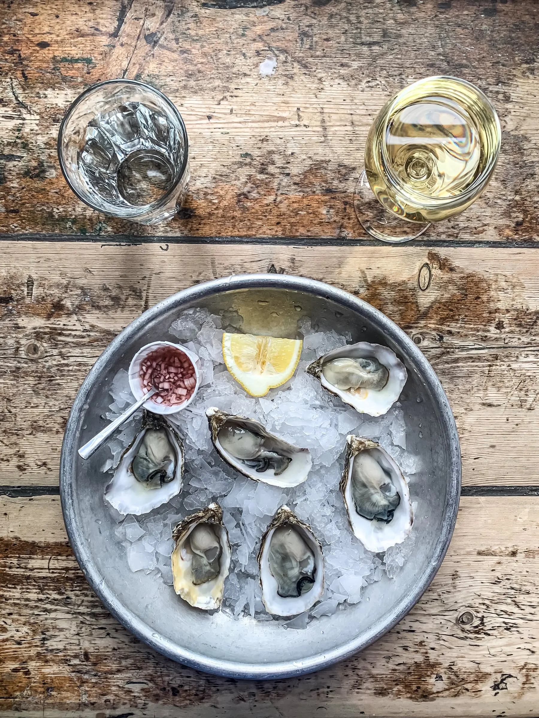 Huîtres ouvertes sur un plateau de glace pilée, avec du citron et une coupelle de vinaigre à l’échalote, sur une table en bois