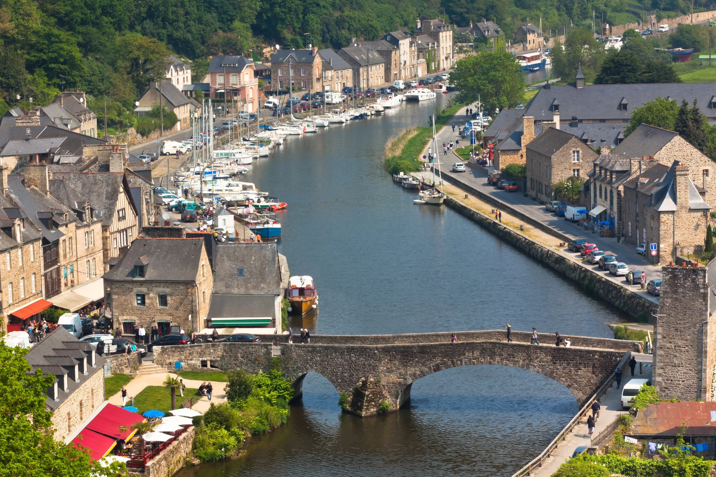 Le port de Dinan au bord de la Rance : bateaux, vieux pont de pierre et maisons anciennes au pied de la vieille ville