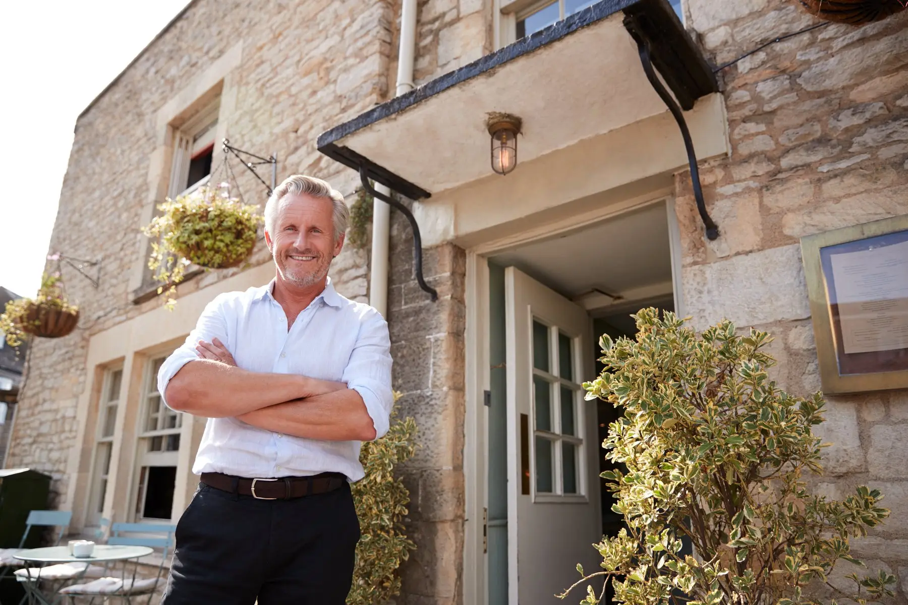 Un hôte souriant devant sa maison en pierre
