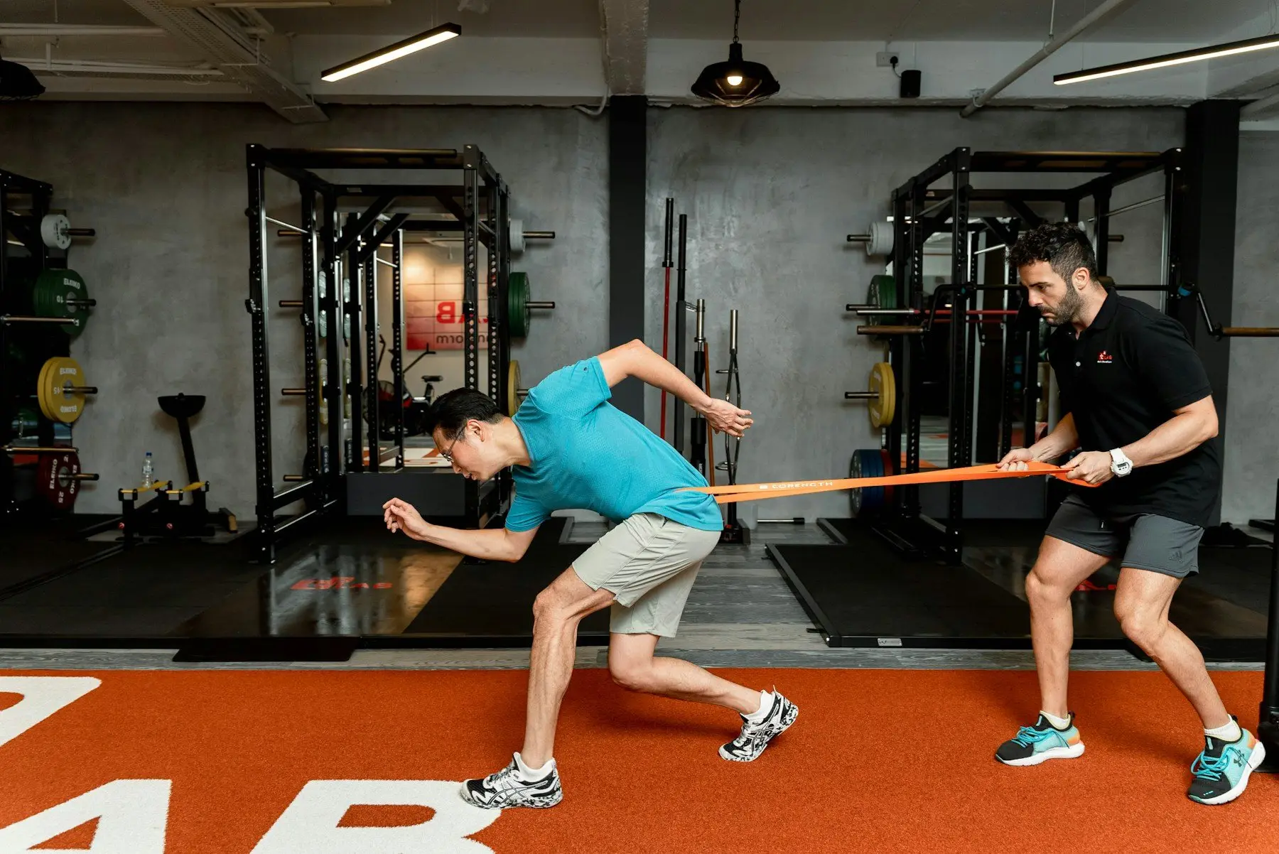 Un kinésithérapeute guide un patient dans un exercice de renforcement avec un élastique, en salle de rééducation
