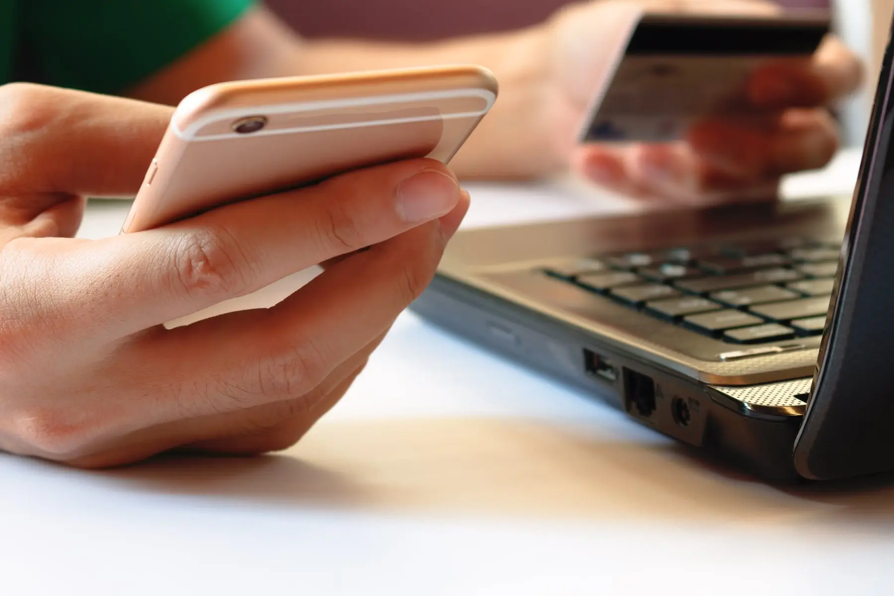 Une main tient un smartphone et l’autre une carte bancaire, devant un ordinateur portable ouvert