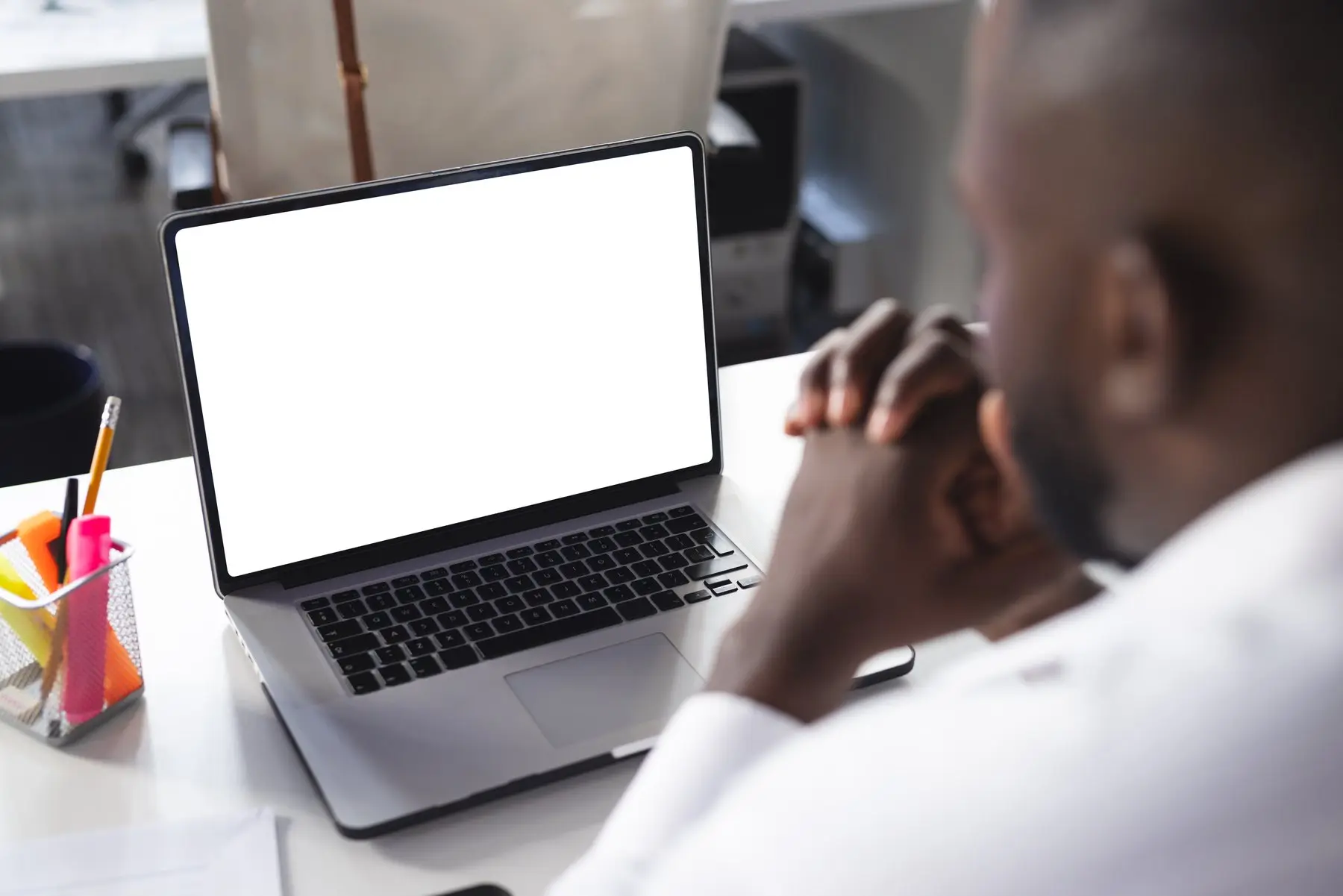 Un homme, les mains jointes, fixe l’écran entièrement blanc de son ordinateur portable posé sur un bureau
