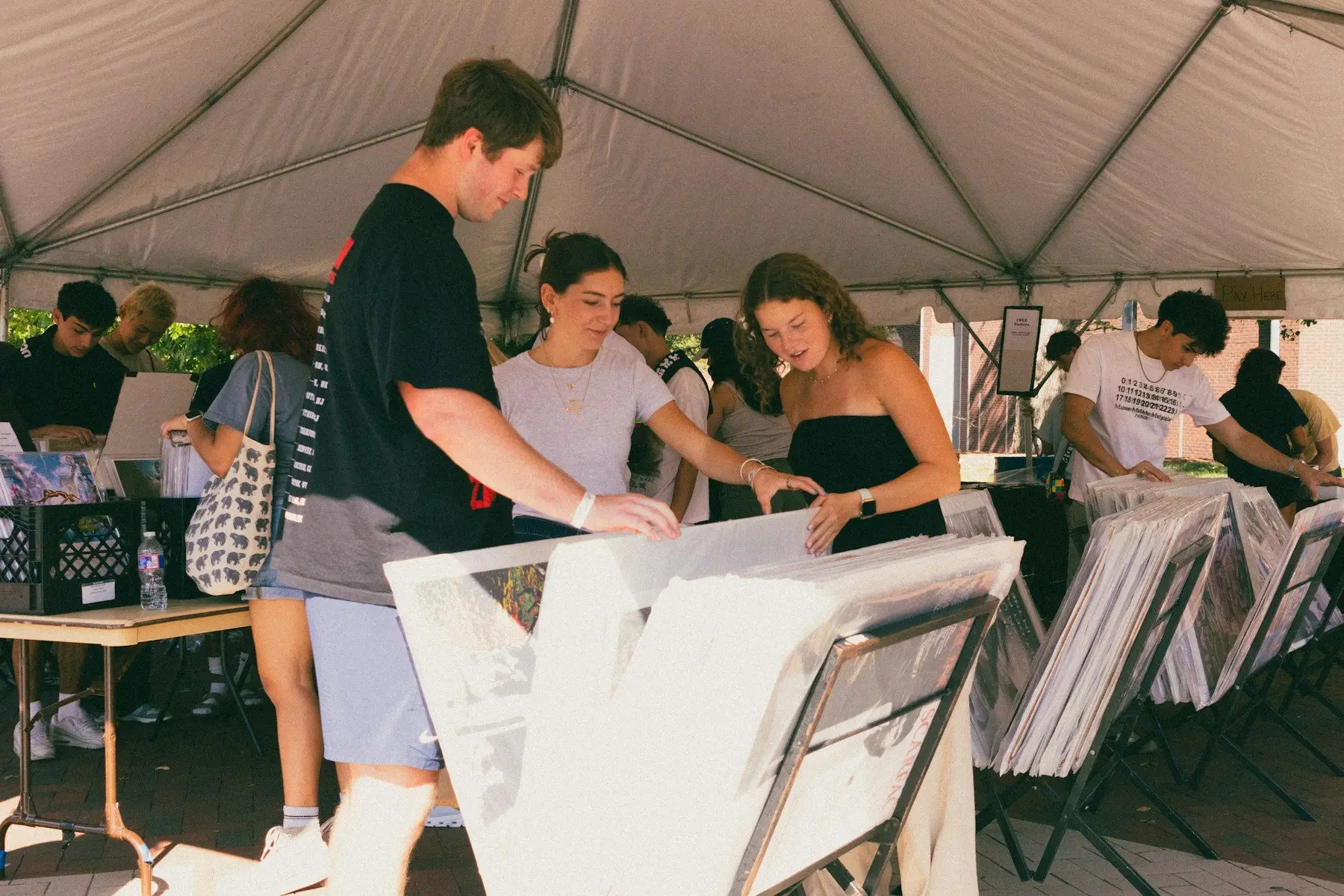 Sous un barnum blanc, des jeunes feuillettent des affiches rangées dans des bacs, lors d’une vente en plein air