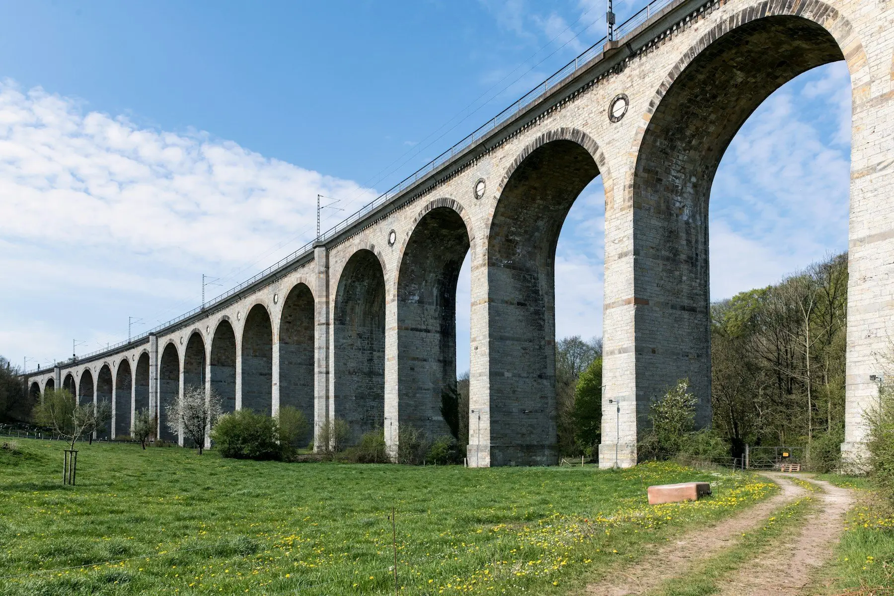 Un viaduc de pierre aux hautes arches enjambe une prairie, un chemin de terre à ses pieds