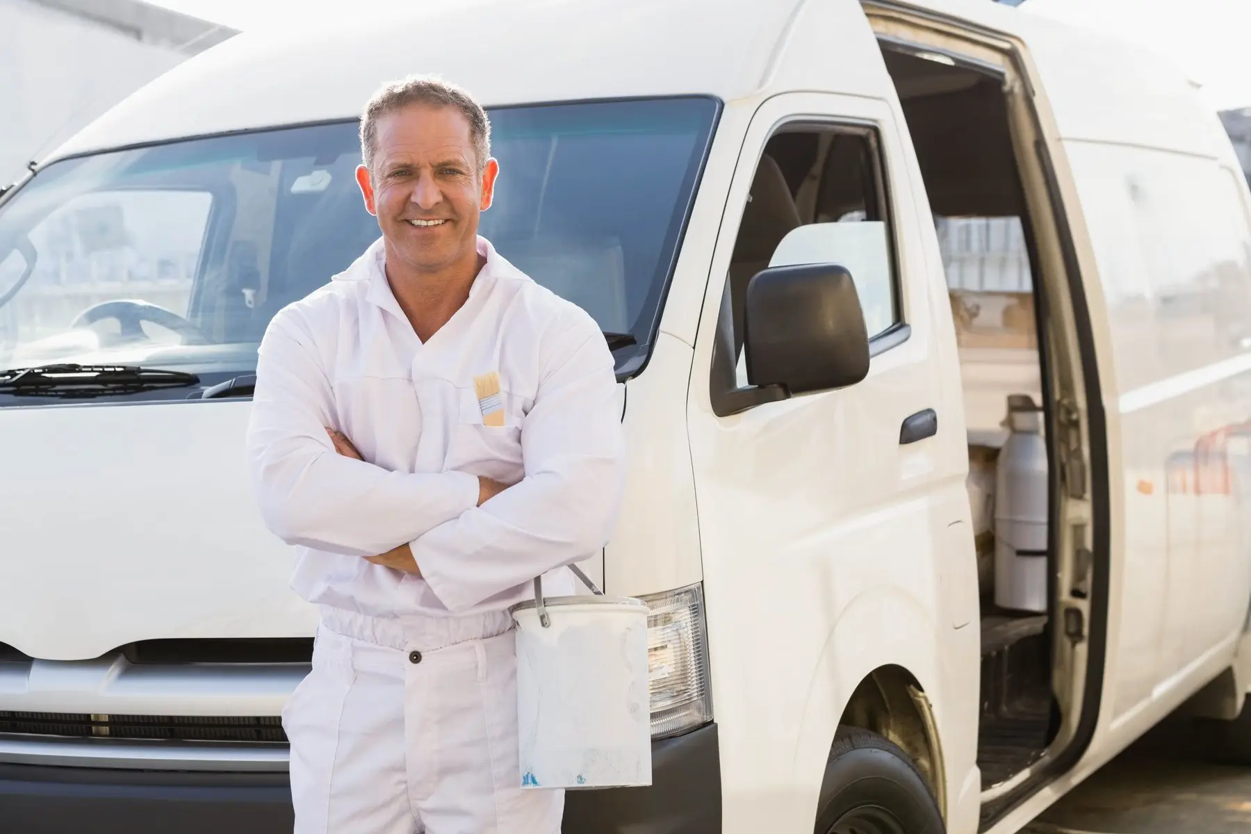 Un artisan peintre en tenue blanche, bras croisés, devant sa camionnette utilitaire
