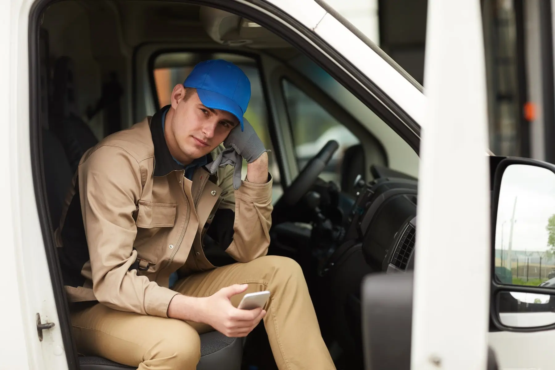 Un livreur assis dans sa camionnette, porte ouverte, regarde son téléphone