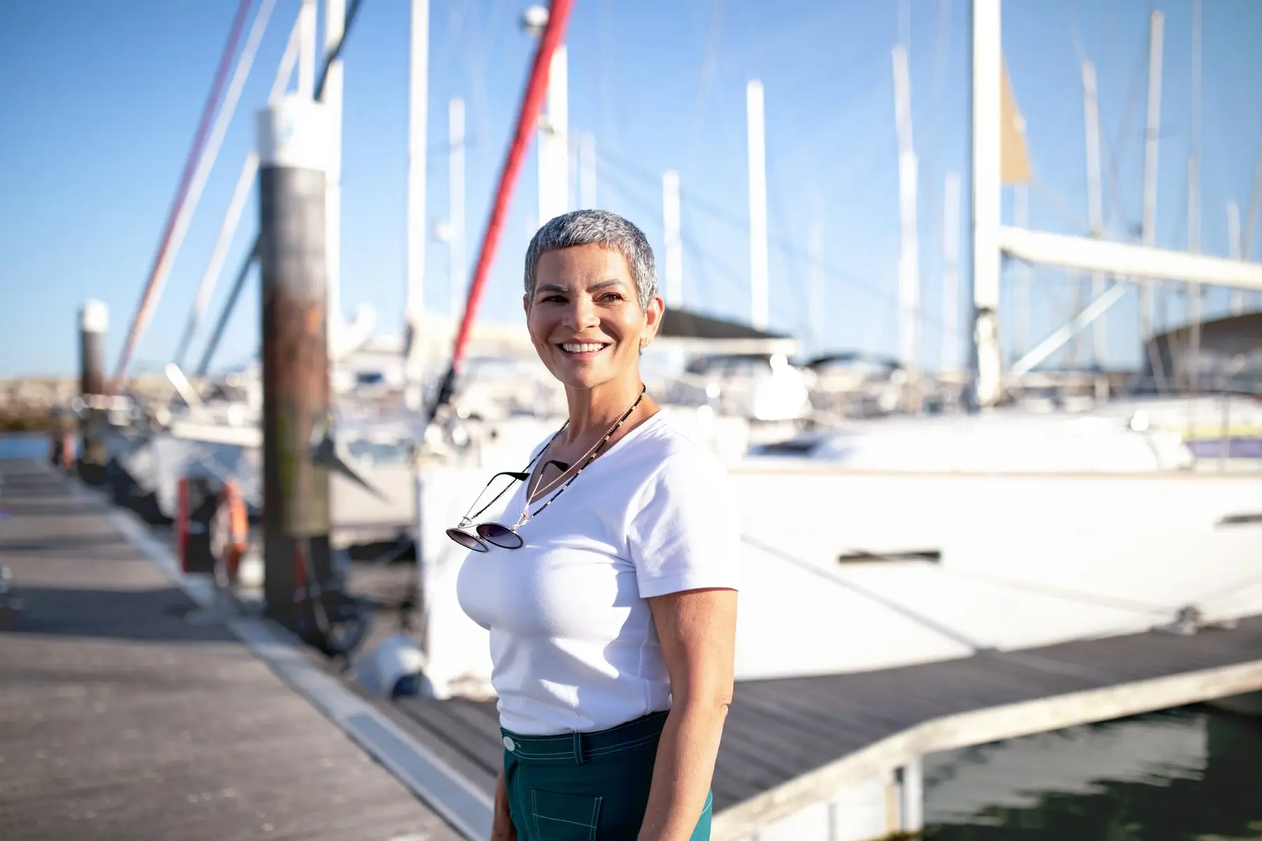 Une femme souriante sur le ponton d’un port de plaisance, voiliers à quai derrière elle